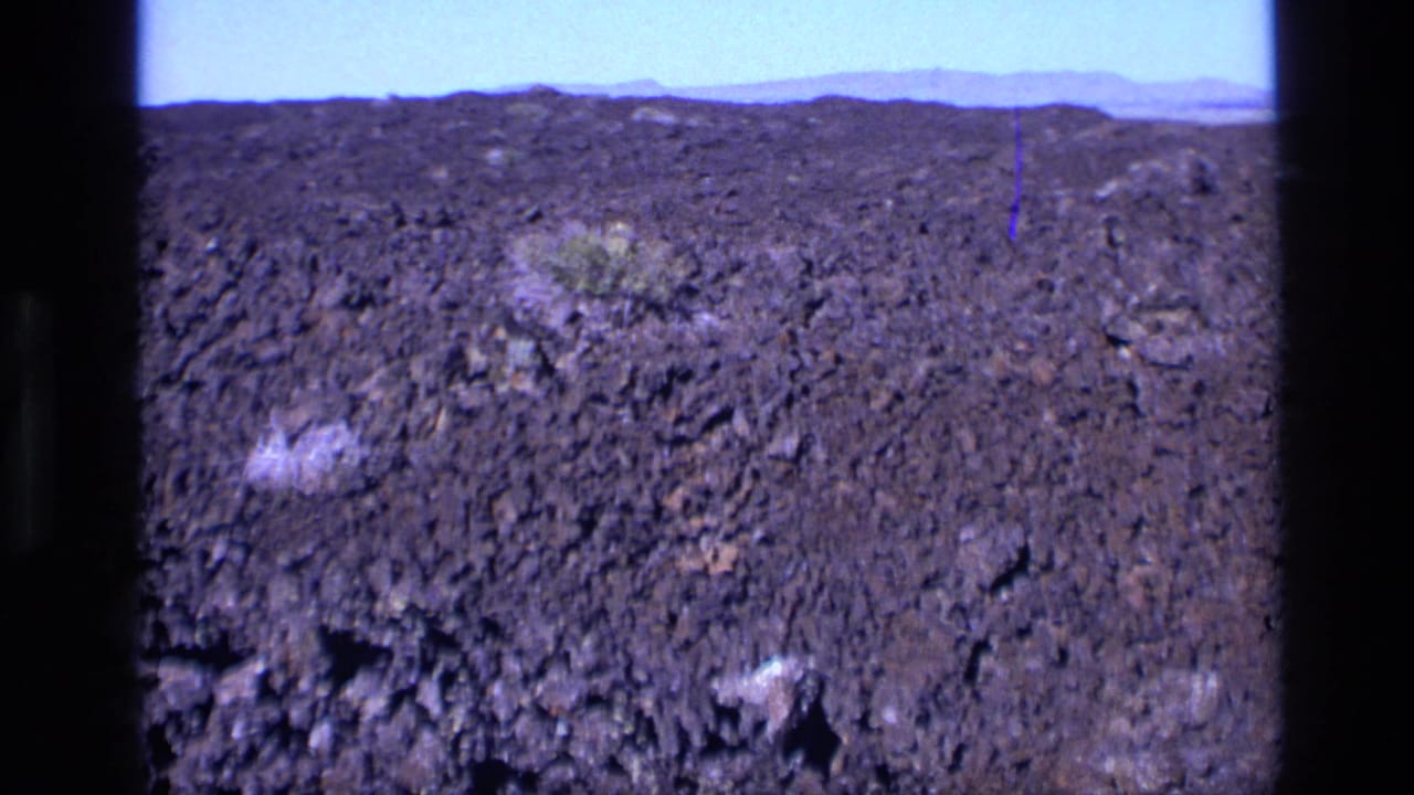 1972 Idaho home-movie frame with rough dark rock spreading to a low horizon and small patches of vegetation.