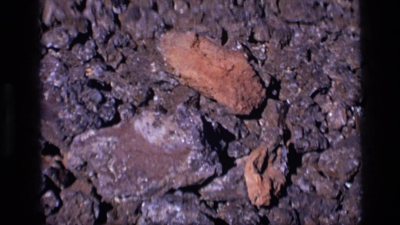 Close-up of dark rocky ground with reddish-brown stone fragments.