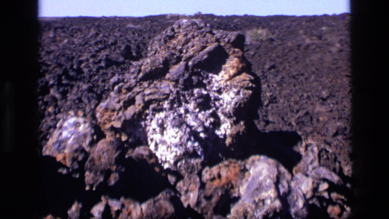1972 Idaho 8mm frame showing a textured volcanic rock formation at Craters of the Moon, with pale deposits and dark lava terrain.