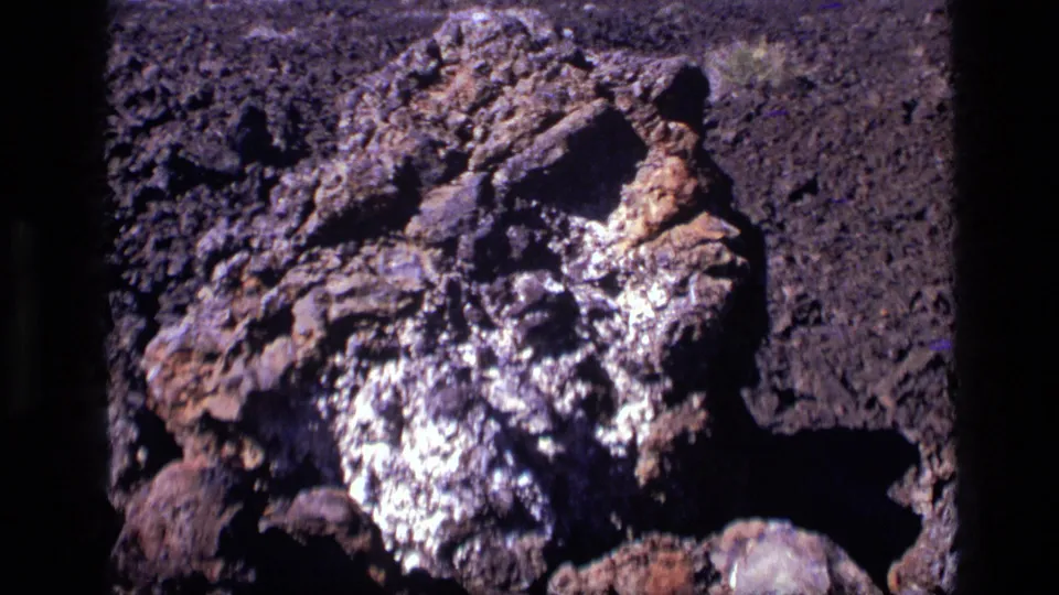 Close 8mm view of the Craters of the Moon rock formation, emphasizing rough texture, pale patches, and shadowed lava stones.