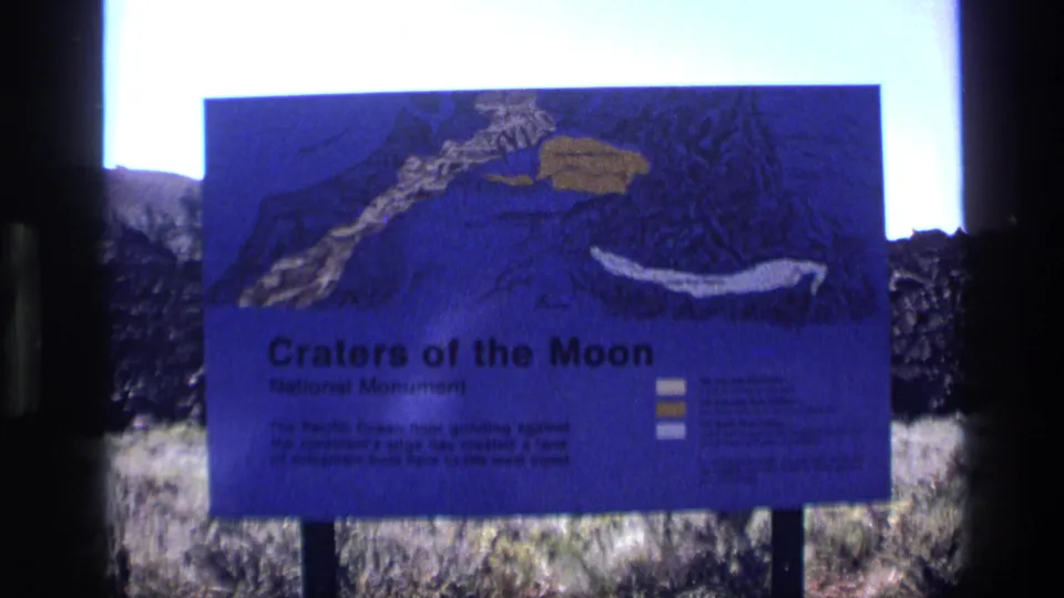 1972 Idaho frame showing a blue Craters of the Moon National Monument interpretive sign set among volcanic rocks.