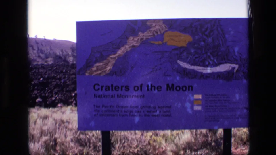 Soft 8mm frame of the Craters of the Moon National Monument sign in Idaho, with saturated color and rugged volcanic ground visible.