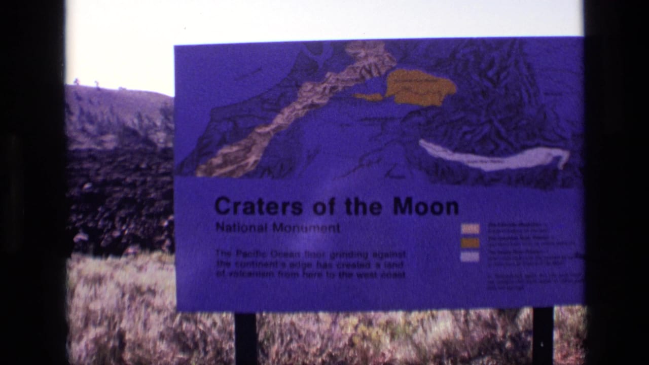 1972 8mm frame of a purple Craters of the Moon National Monument interpretive sign in Idaho, seen partly through dark film borders.