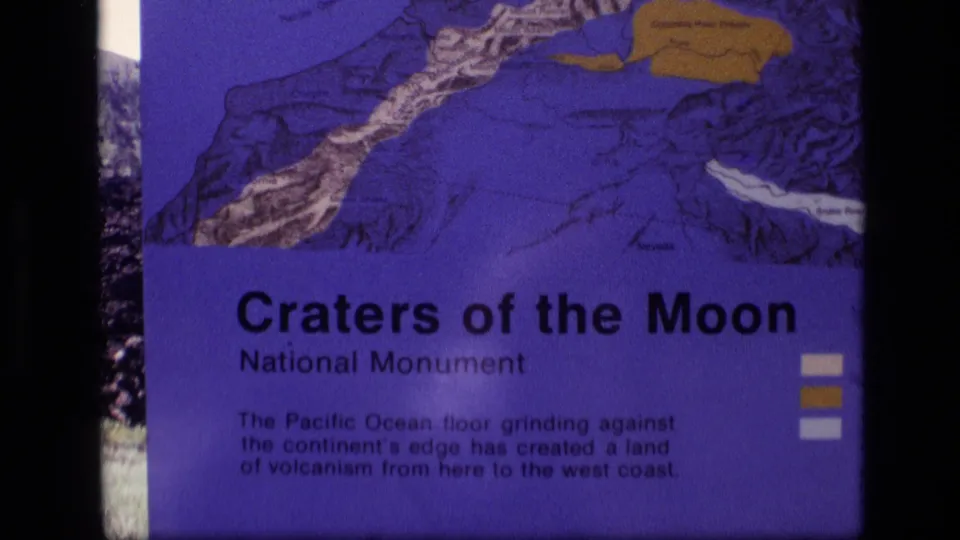 Centered 1972 8mm frame of the Craters of the Moon National Monument interpretive sign in Idaho, with outdoor landscape behind it.