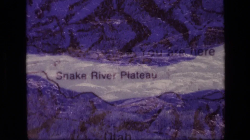 Transition frame where the Snake River Plateau map remains visible through a darker exposure shift on 1972 8mm footage.