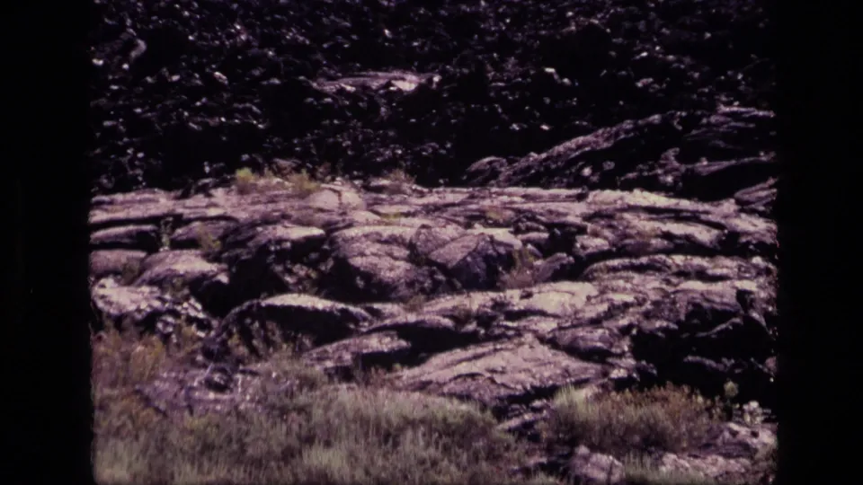 Rocky Idaho terrain with dark stone, scrubby grass, and dry vegetation, filmed on 8mm after the Snake River Plateau map.