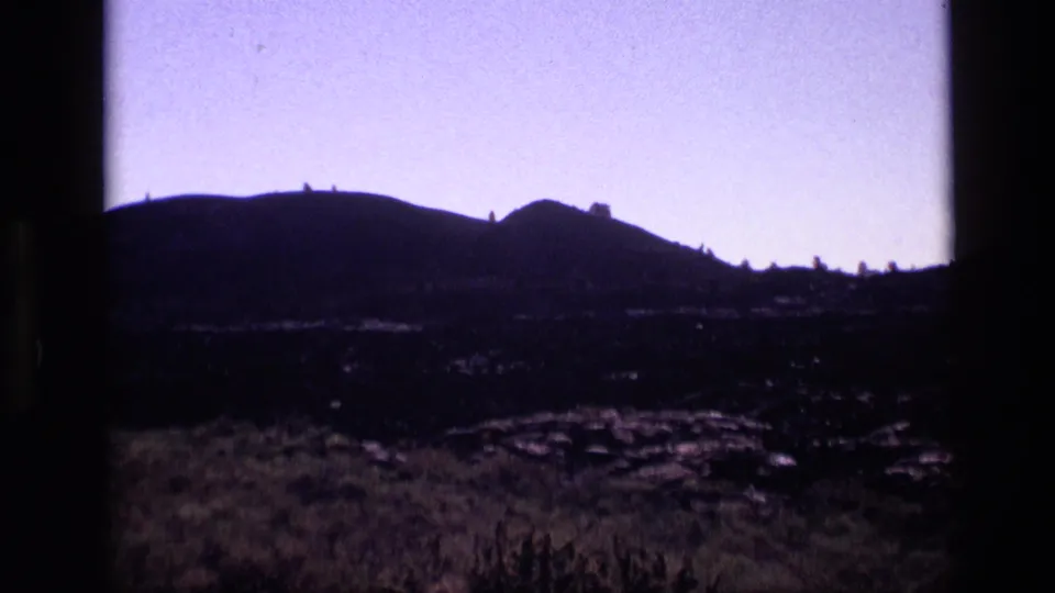 1972 Idaho 8mm frame showing burned ground, sparse grasses, and a dark hill silhouette beyond the field.