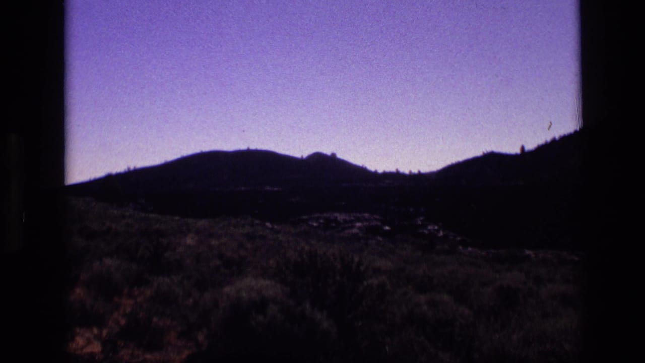 1972 Idaho 8mm landscape frame with a low mountain silhouette, violet sky, and shadowed desert scrub.