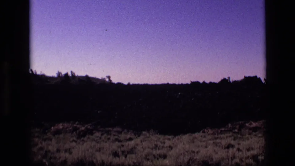 1972 Idaho 8mm frame showing a darker desert foreground, low brush, and pale violet sky near sunset.
