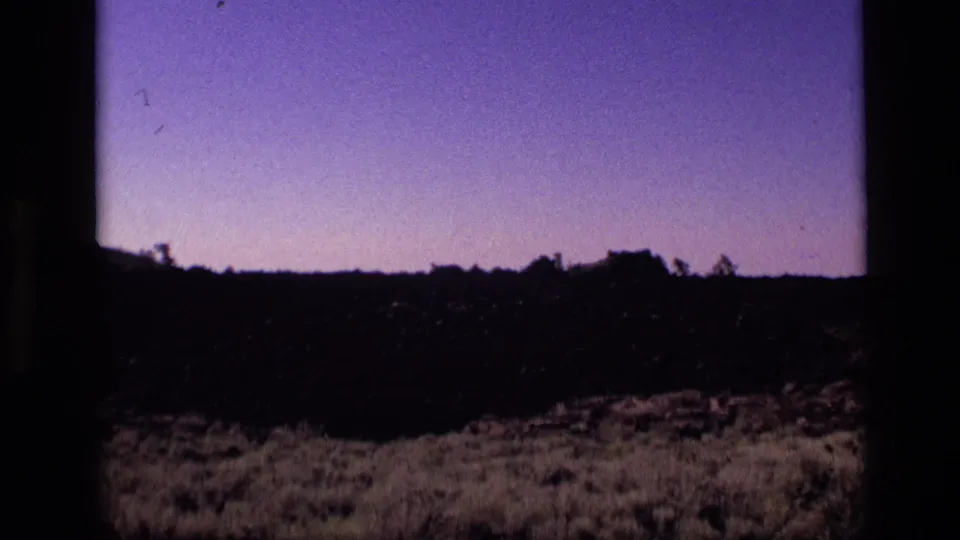 1972 Idaho 8mm landscape frame with silhouetted scrub, uneven terrain, and a fading purple twilight sky.