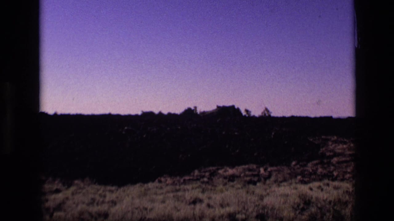Dark rocky ridge beneath a purple sky with sparse trees along the horizon.