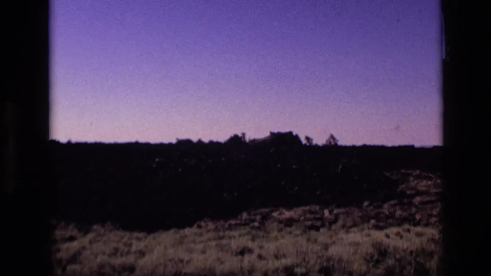 1972 Idaho 8mm frame showing a dark rocky ridge, scrub, and sparse trees silhouetted below a purple sky.