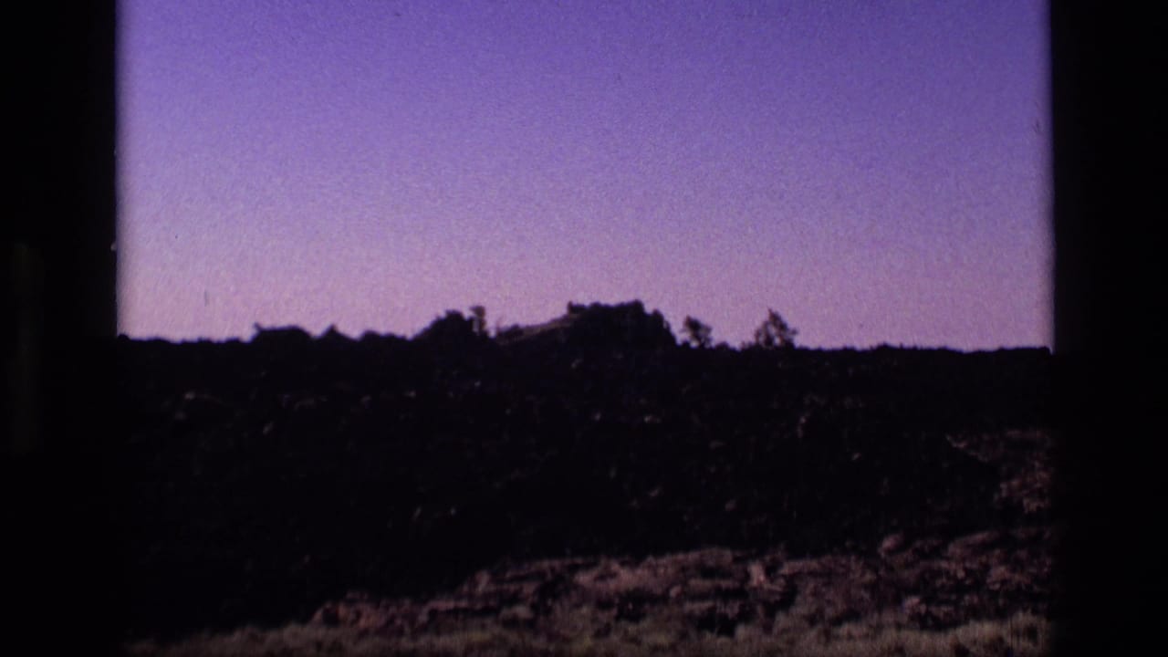 1972 Idaho home-movie still with a dark rocky horizon, sparse vegetation, and purple-tinted sky.