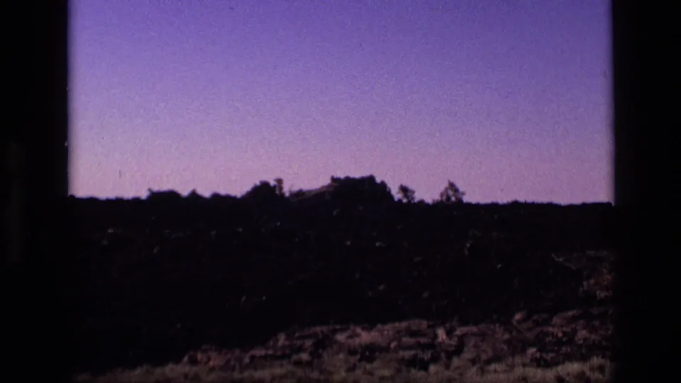 1972 Idaho home-movie still with a dark rocky horizon, sparse vegetation, and purple-tinted sky.