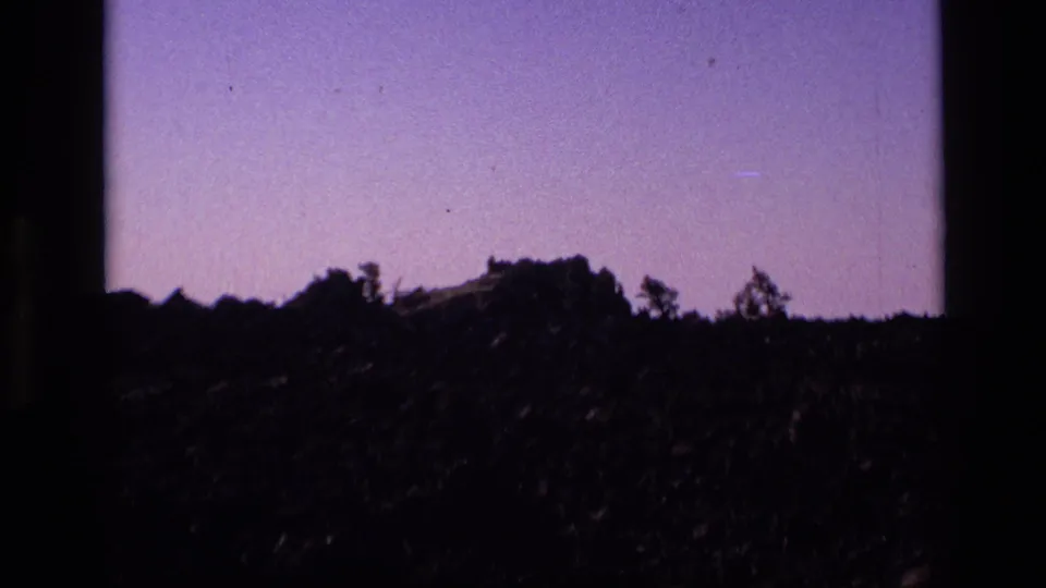 1972 Idaho 8mm still showing a low rocky hill and scattered trees against a pale purple sky.