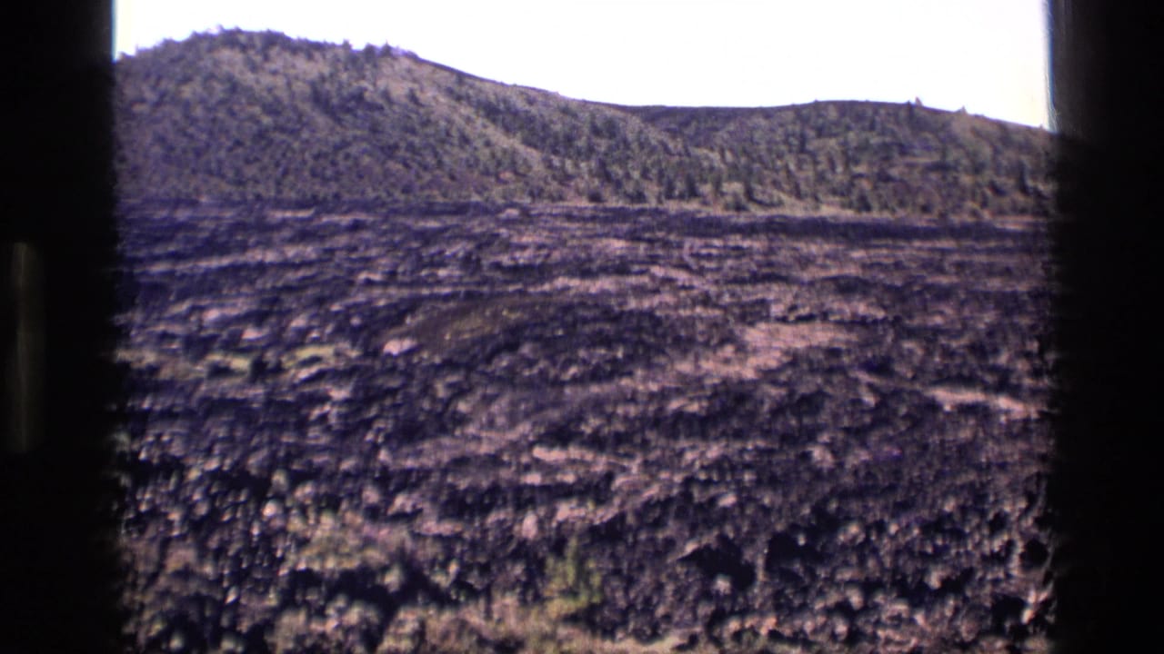 Rocky dark ground and green hillside seen through film-frame edges.