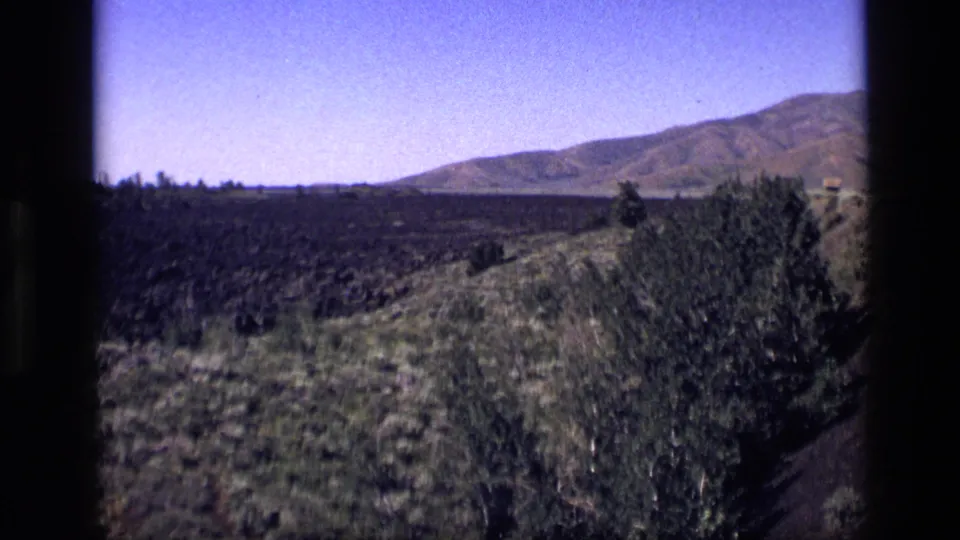 1972 Idaho 8mm frame showing dry grasses, shrubs, rolling hills, and distant mountains under a bright sky.