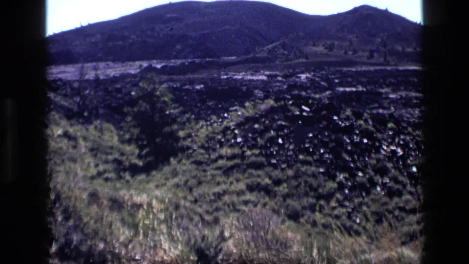 1972 Idaho home-movie view of dark ground cover, dry grass, and a mountain ridge framed by 8mm borders.