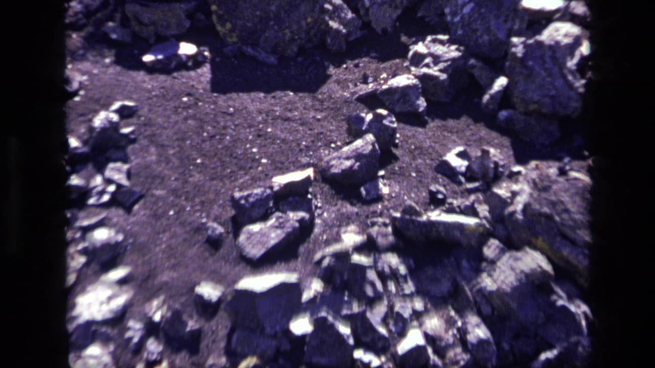 1972 8mm Idaho footage showing dark lava rocks and gravel in a close visitor-shot view with visible film borders.