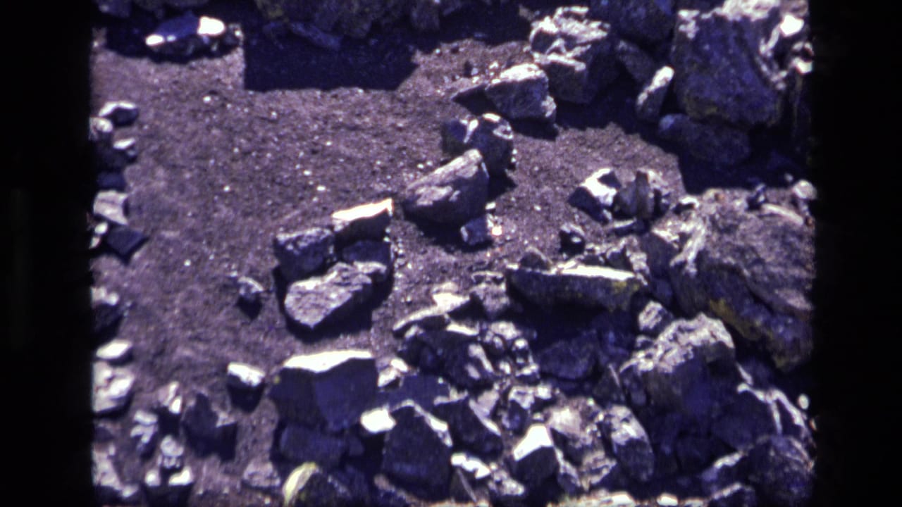 Close 8mm view of Idaho volcanic rocks and gravel, with aged color shift and a central film-frame divider visible.
