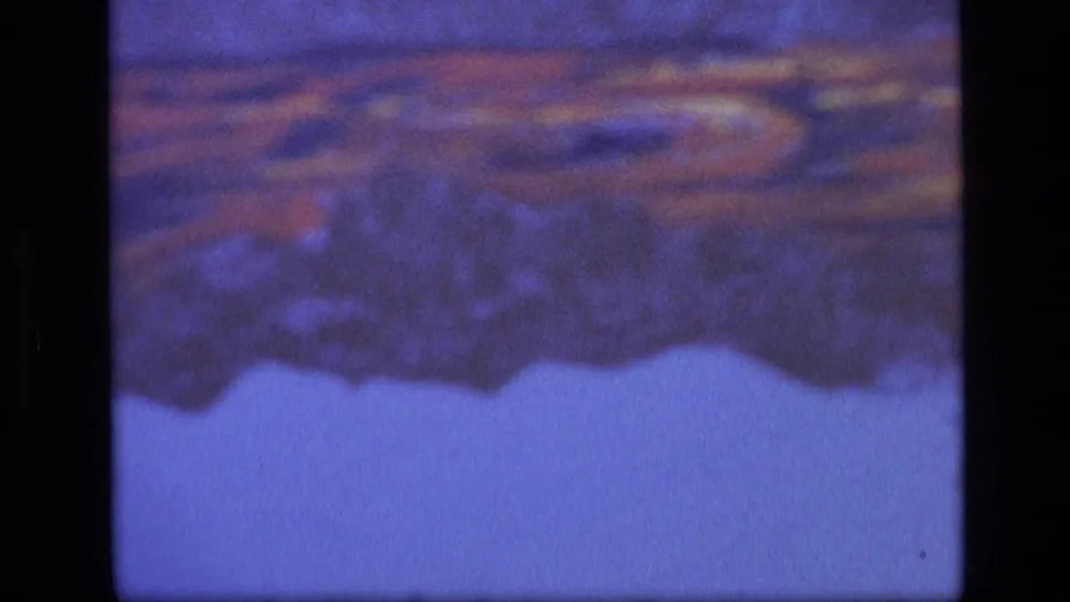Soft 1972 8mm frame showing part of an illustrated sign or placard, with orange bands above a pale blue area.
