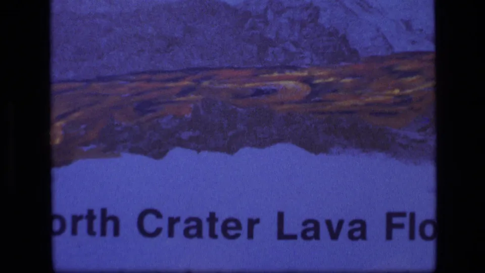 1972 Idaho 8mm frame showing a partial North Crater Lava Flow sign or placard with illustration and cropped text.