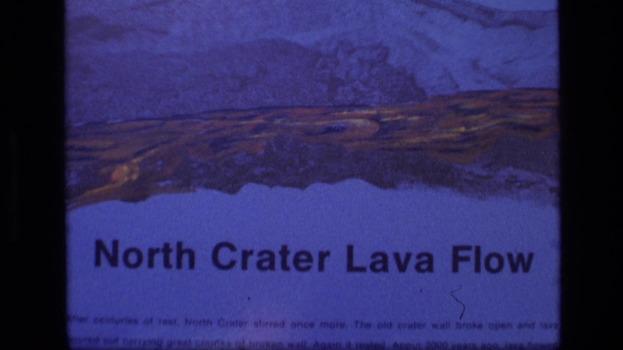 Close view of a sign titled North Crater Lava Flow with a painted volcanic landscape above the text.