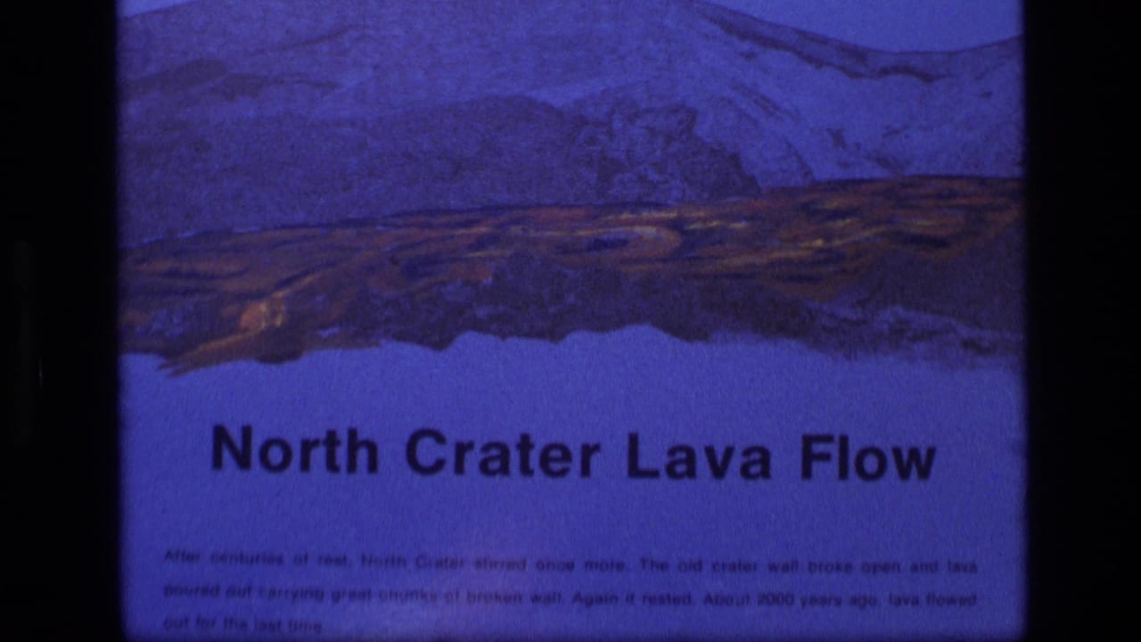 1972 Idaho 8mm frame showing a North Crater Lava Flow informational sign with illustrated volcanic terrain and small text.