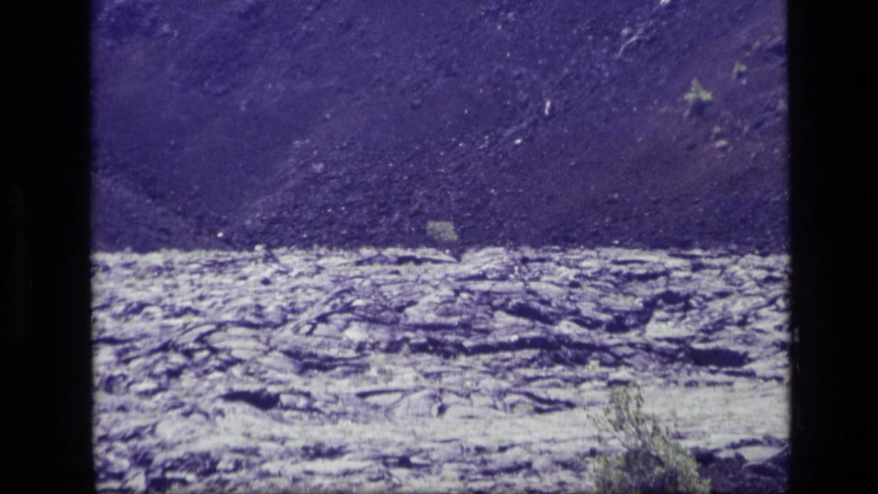 Dark lava field in front of a steep volcanic slope under a deep blue-purple sky.