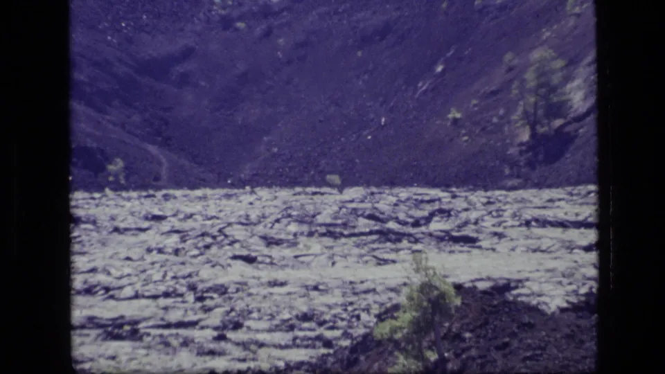 1972 8mm home-movie frame from Idaho showing a pale lake below dark rolling hills with sparse vegetation in front.