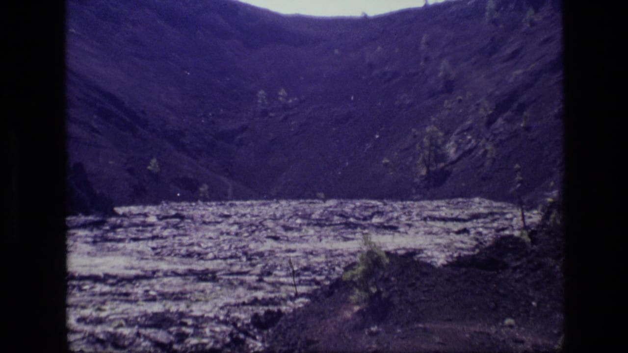 Idaho landscape frame from 1972 8mm footage, showing a wide pale lake set between dark hills and sparse brush.