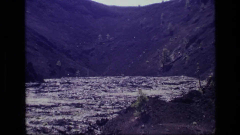 Idaho landscape frame from 1972 8mm footage, showing a wide pale lake set between dark hills and sparse brush.