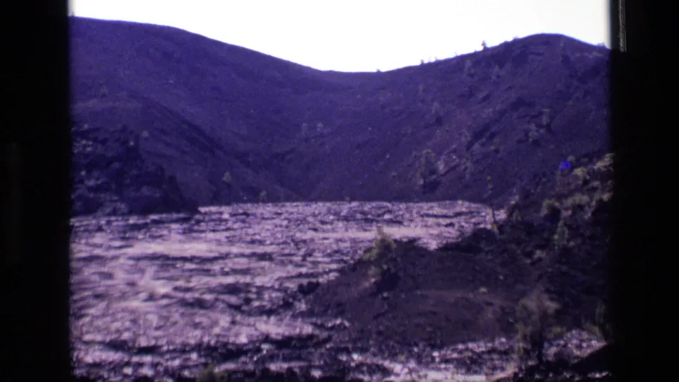 1972 Idaho 8mm frame showing rolling hills behind a bright, rippled lake and rough foreground terrain.