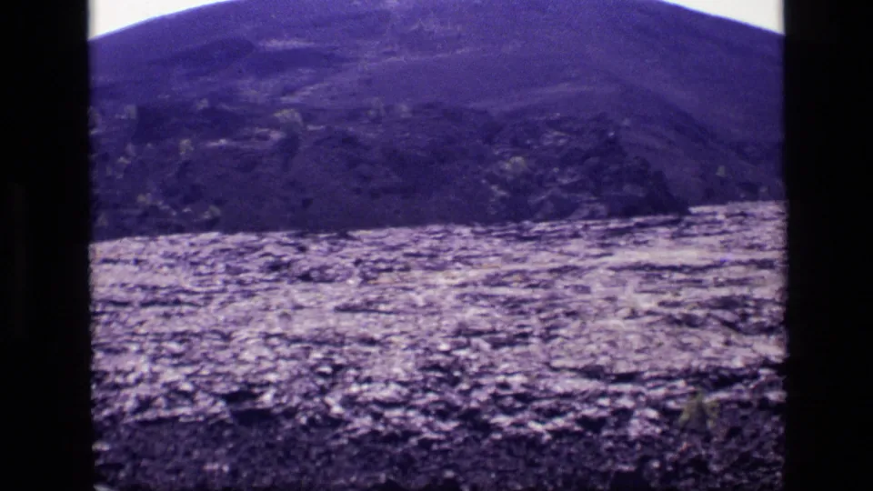 1972 Idaho 8mm frame with rolling hillside, uneven rocky ground, sparse plants, and bright overexposed sky during the camera pan.