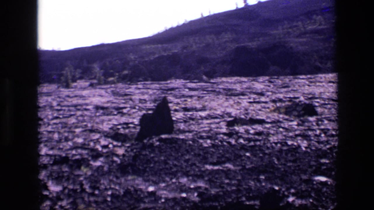 Barren dark volcanic field with low hills and a large rock shape in the foreground.