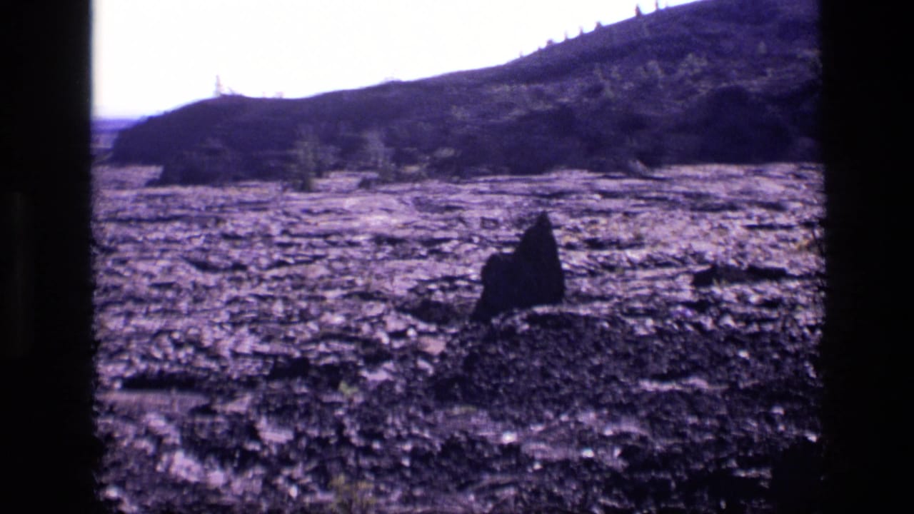 Wide volcanic field with a dark foreground rock and hills along the horizon.