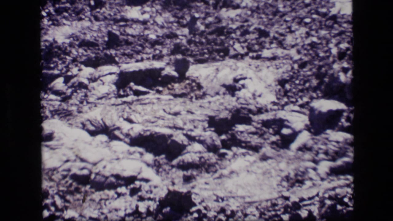 1972 Idaho 8mm frame showing close-up rugged rock formations with cracked, layered surfaces and shadowed crevices.