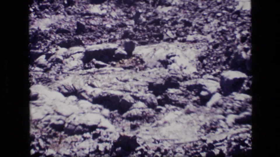 1972 Idaho 8mm frame showing close-up rugged rock formations with cracked, layered surfaces and shadowed crevices.