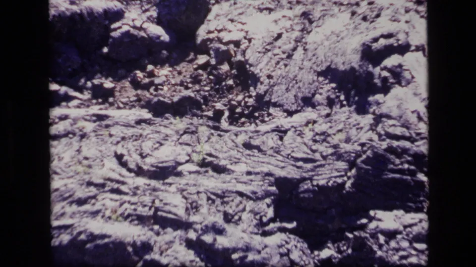 1972 Idaho 8mm frame showing rugged cracked rock, scattered stones, and a dark raised formation near the lower right.
