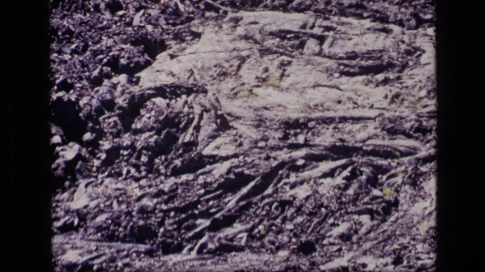 1972 Idaho 8mm frame showing pale solidified lava surrounded by darker rubble and sparse vegetation on rough volcanic ground.