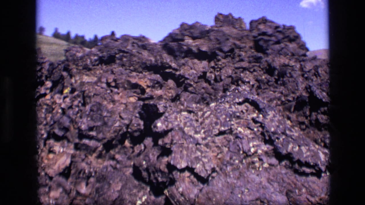 1972 Idaho 8mm frame showing a close view of rugged dark rock under bright blue sky.