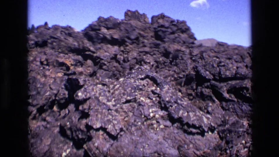 1972 Idaho 8mm frame with a rugged rock ridge, distant hills, and a small cloud in blue sky.