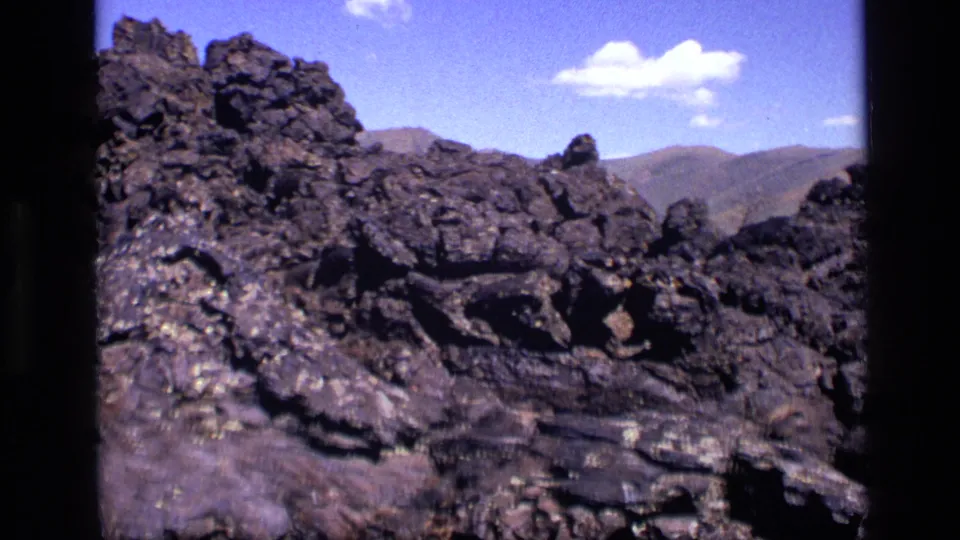 1972 Idaho 8mm frame showing a jagged rock outcrop, distant hills, and small white clouds.