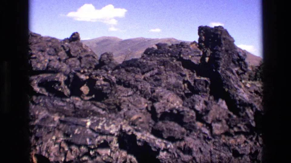 1972 Idaho 8mm landscape frame showing a lava-rock field, a taller jagged outcrop, and distant mountain ridges.