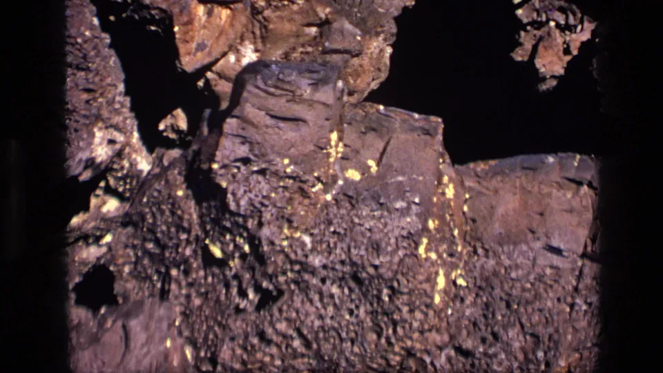 Close 1972 Idaho 8mm view of textured volcanic rock, yellow-green lichen, and dark crevices in strong sunlight.
