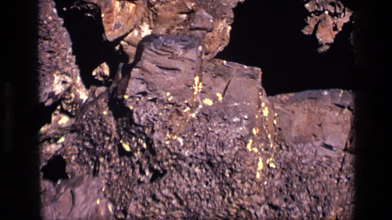 Close-up of rough rock with small golden flecks against a dark background.