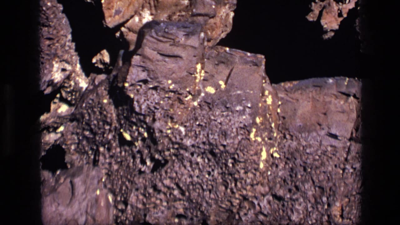 1972 Idaho 8mm frame with jagged brown rock, small yellow metallic flecks, and dark framing around the close-up subject.
