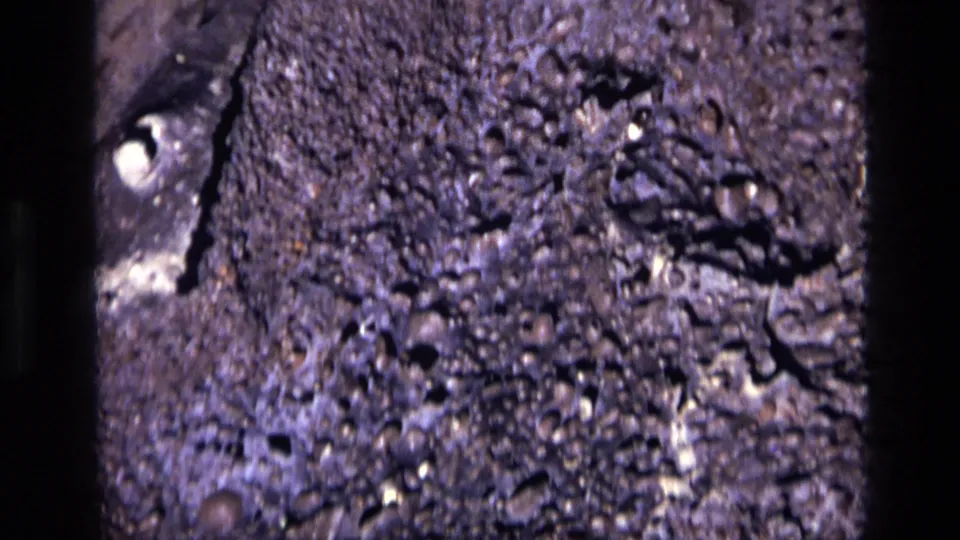 Close 1972 Idaho home-movie view of pitted gray rock, showing pale mineral marks and irregular shadowed holes.