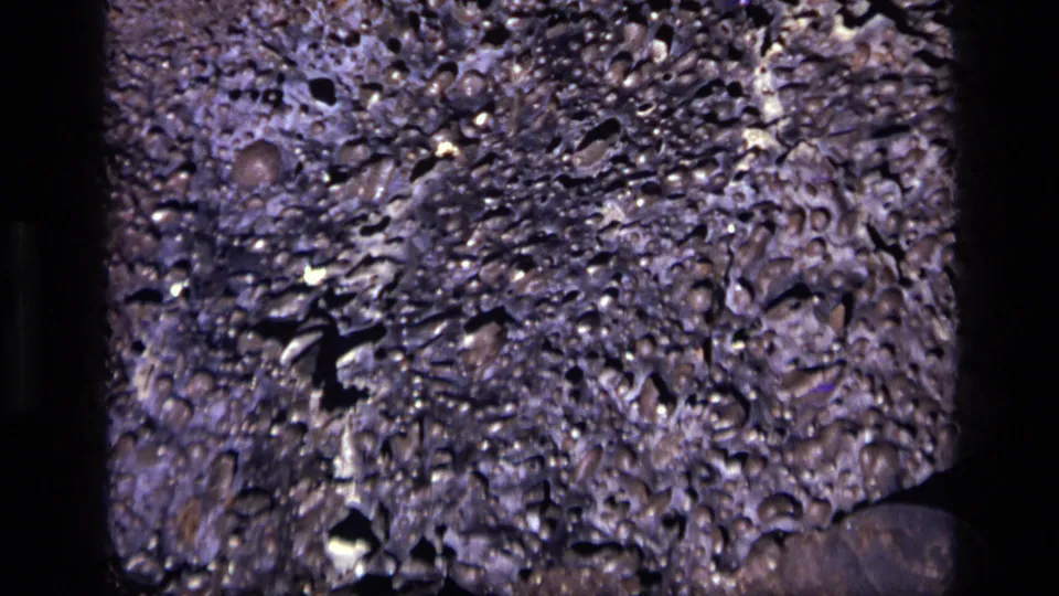 Final 1972 Idaho 8mm close-up showing rough gray-white rock with porous holes, bright flecks, and a darker lower corner.