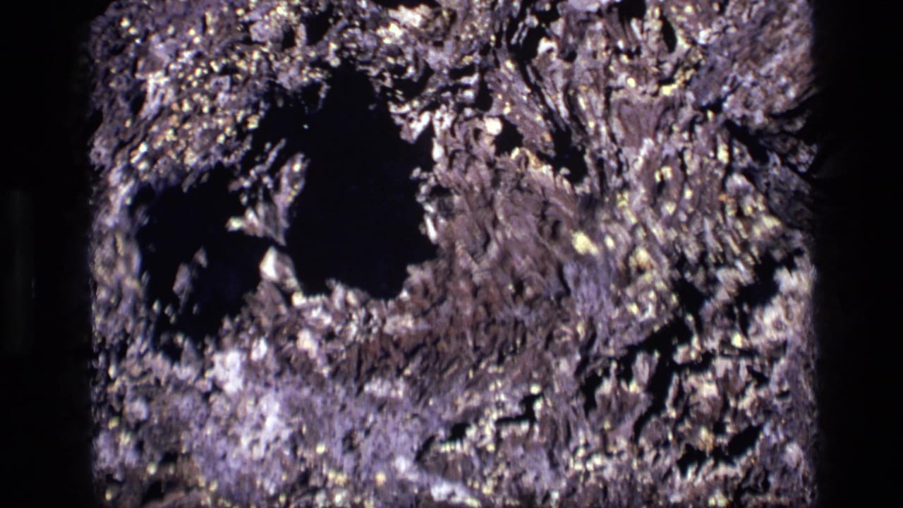1972 Idaho 8mm frame with a dark hollow area surrounded by rough, brittle-looking ridges and pale flecks.